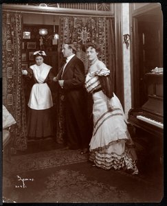 正式な服装の男性と女性、ピアノのある部屋で家事のように見えるもの、1905年（銀ゼラチンプリント）